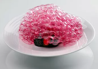 The image showcases a vibrant dish of edible pink bubbles, delicately dispensed atop a bed of sun-ripened berries. The bubbles, infused with the earthy sweetness of beetroot, create a voluminous dome that glistens enticingly. The dish is garnished with edible flowers, adding an extra layer of visual allure.
